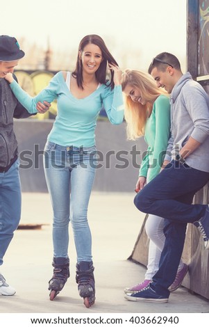 Group of teenagers having fun in a skate park  helping their friend to learn to roller skate