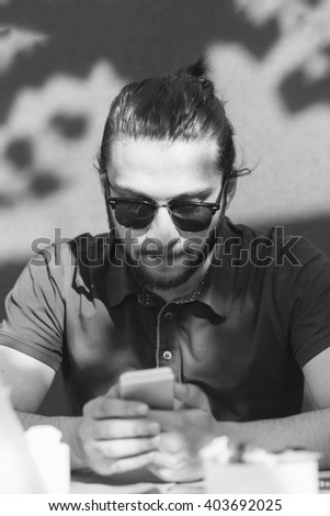 Photo bearded businessman relaxing modern loft office. Banker sitting in vintage chair, looking mobile phone. Using contemporary smartphone. Blurred background. Wide, film effect.
