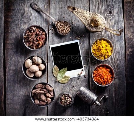 Spices, pepper grinder, blank photo frame and dry red chili peppers at grey wooden background with spoons nearby