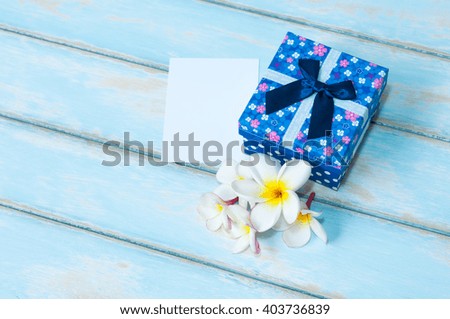 Blue gift box and card with flower on sky blue color wooden floor.