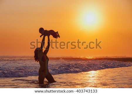 Happy family swimming fun on sea beach - mother tossing up baby son into mid air, catching on sunset sky, sun background Parents outdoor activity, child lifestyle on summer vacation in tropical island