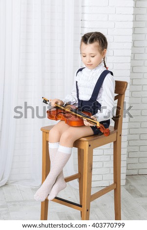 little girl sitting on a chair with a violin and looking at her