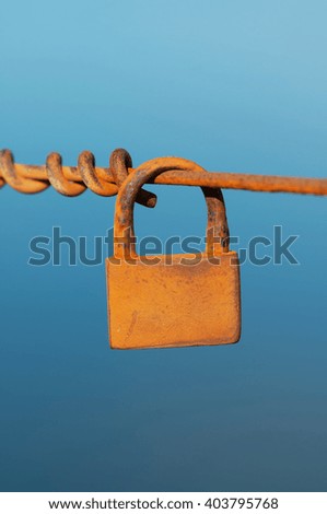 Old rusty padlock hanging from a metal cable against a blue sky. Selective focus.
