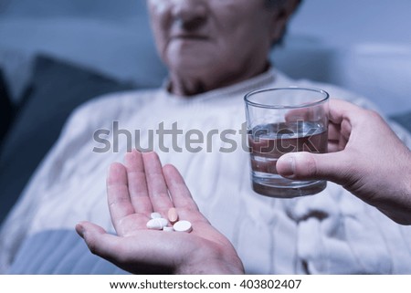 Cropped picture of a person holding some pills and a glass of water