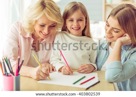 Granny, her daughter and granddaughter are drawing and smiling while sitting at home