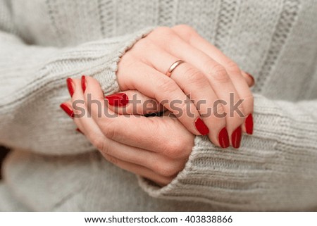 Bright manicure on female hands. Woman in a gray knitted sweater shows red manicure closeup.