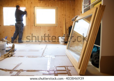 Worker in the background installing new, three pane wooden windows in an old wooden house, with a new window in the foreground. Home renovation, sustainable living, energy efficiency concept. 
 Royalty-Free Stock Photo #403846939