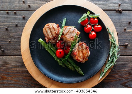Grilled pork dish with fresh vegetables. Food photography of grilled pork medallions with herbs and spices. Tasty cook meat with  vegetables on dark wooden background. 