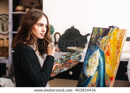 Creative pensive  painter paints a colorful picture. Closeup of painting process in art workshop Creative positive woman painter paints in her studio abstract picture. 