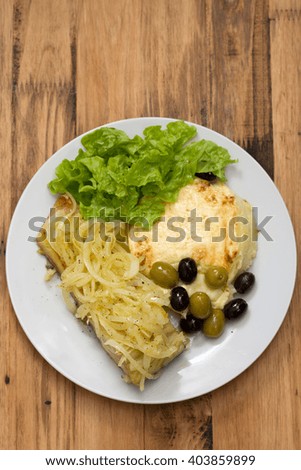 cod fish with onion, mashed potato and lettuce on white plate on brown wooden background
