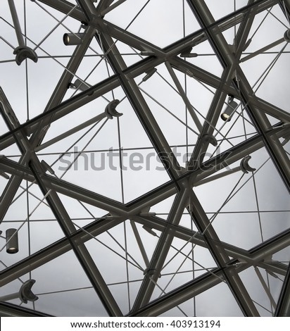 Double exposure photo of modern structural glass ceiling with cable track lighting system of halogen lamps inclined at various angles. Abstract fragment of hi-tech architecture / interior.