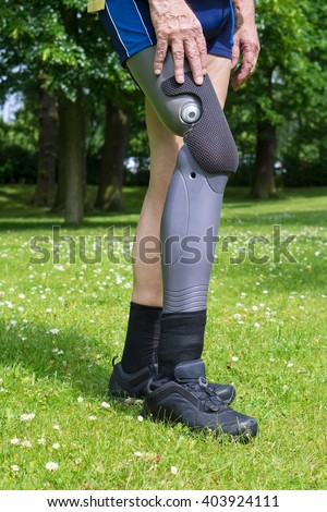 Close up side view on gray plastic prosthetic leg of single man in yellow shirt and blue shorts walking in green grass with white clover flowers Royalty-Free Stock Photo #403924111