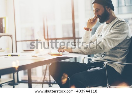 Picture bearded art director working with new project modern loft. Using contemprary notebook on wood table. Thinking idea. Freelance world. Blurred background, film effect