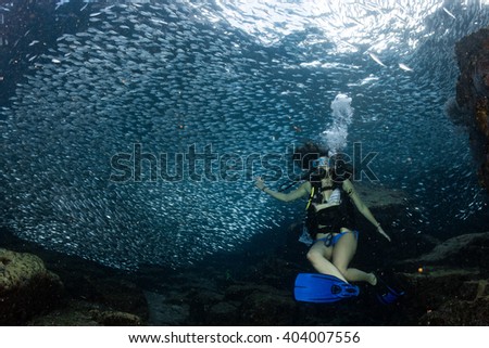 Black hair young and pretty mexican latina Scuba diver while going Inside a giant sardines school of fish bait ball in the reef and blue sea