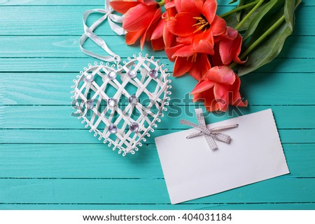 Fresh coral tulips, decorative heart and empty tag  on teal  painted wooden background. Selective focus. Place for text.