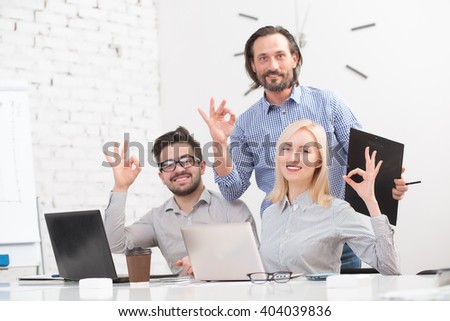 Business people showing okay signs in office while working on laptop computer and discussing business projects.