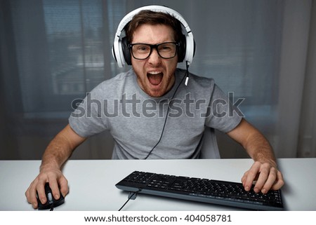 technology, gaming, entertainment, let's play and people concept - angry screaming young man in headset with pc computer playing game at home and streaming playthrough or walkthrough video Royalty-Free Stock Photo #404058781