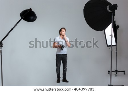 Pensive male photographer standing in professional studio with equipment