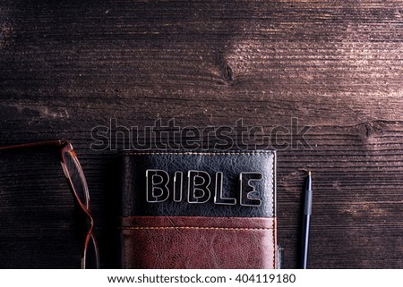 Bible, eyeglasses and pen laid on old wooden table