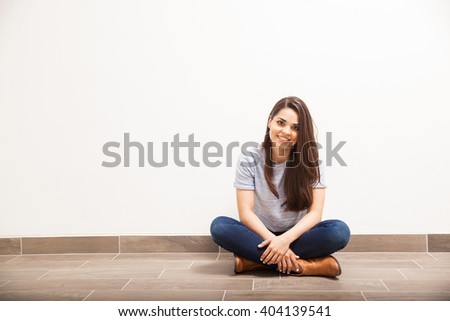 Good looking young Latin woman relaxing and sitting on the floor against a white wall and smiling. Lots of copy space