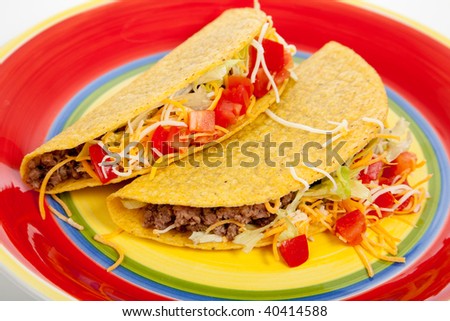 Two tacos on a red plate with tomatoes, beef, lettuce and cheese