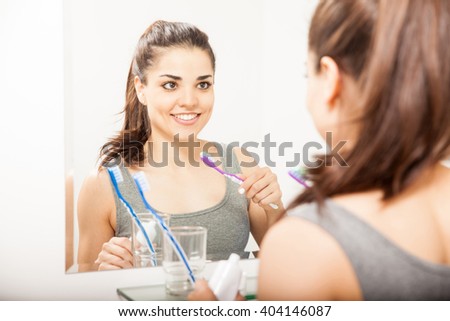 Attractive young woman holding a toothbrush and smiling in front of a mirror in the bathroom