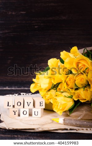 Wooden cubes with inscription "LOVE YOU" and bouquet of yellow flowers on vintage paper, wooden background. Selective focus.