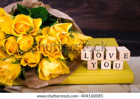 Wooden cubes with inscription "LOVE" and bouquet of yellow flowers on vintage paper, wooden background. Selective focus.