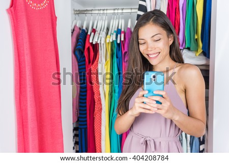 Shopping girl taking selfie in mirror of changing room at store or home walk-in closet in bedroom. Asian woman taking a photo of her outfit texting sms on social media using smart phone fashion app.