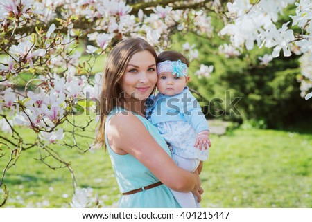 Beautiful mother with dark hair posing with her little cute baby in blossom garden
