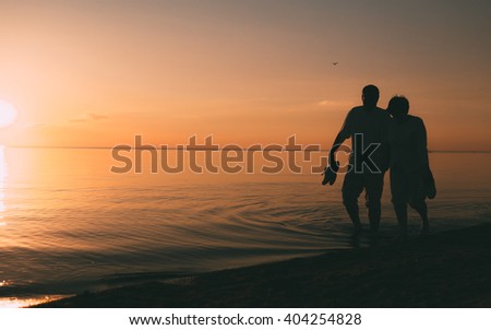 Silhouette of adult couple walks on the seashore against a sunset. Evening photo.