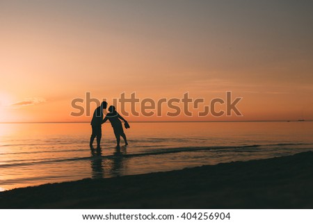 Silhouette of adult couple standing in water want to kiss against a sunset.
