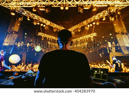 DJ hands up at night club party under yellow lasers with crowd of people Royalty-Free Stock Photo #404283970