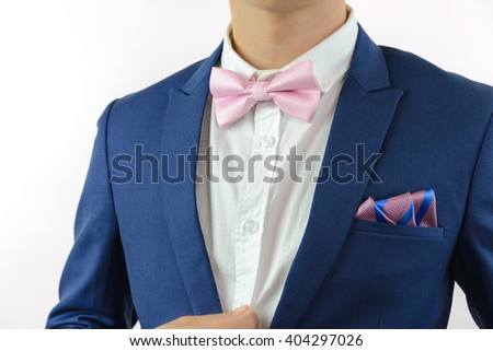 Man in blue suit with pink bow tie, flower brooch, and pink blue strip pocket square, close up