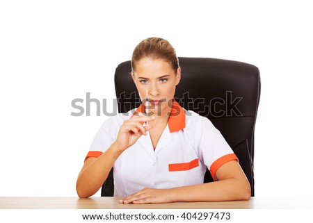 Young female doctor or nurse sitting behind the desk and holding syringe