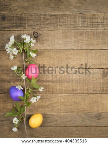 Bright, Colorful Easter Eggs on side and bottom of Rustic Wood Boards Background with blank room or space for copy, text, your words and with white spring flowers. Vertical aerial top view