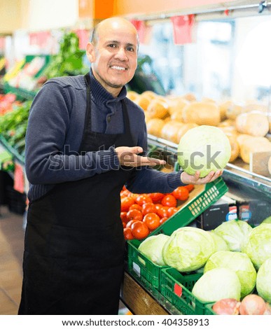 Charming salesman posing near display with different vegetables  in supermarket 
