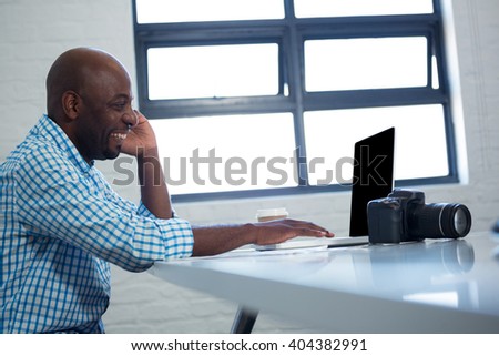 Man talking on mobile phone while using laptop in office