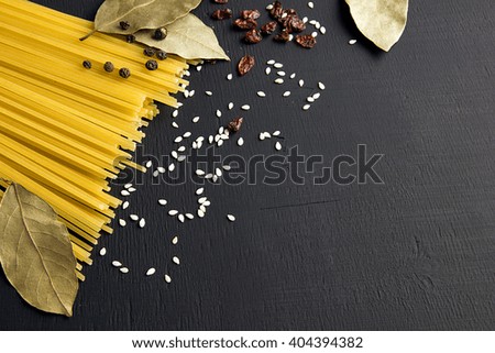 Raw spaghetti and Bay leaf, barberry, pepper, sesame seeds on black wooden background, top view place for text