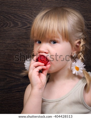 Funny little girl eating a strawberry. Portrait, face close. Blond hair, pigtails. Strawberries ripe, red. Girl grubby and rather