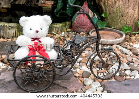 white teddy bear holding present on bicycle in garden background, love concept for valentines day