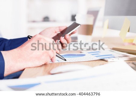 Sideview of businessman using cellphone over business charts in office