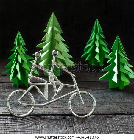 Healthy lifestyle concept. Metal figures cyclists and paper spruce origami as an illustration sports. Selective focus, square image