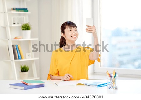 people, education, high school and learning concept - happy asian young woman student taking selfie with smartphone at home
