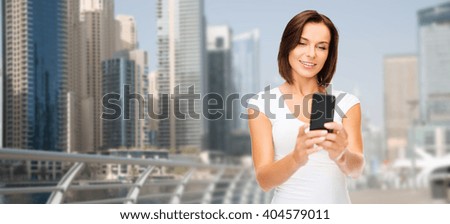travel, tourism, summer vacation, technology and people - happy young woman taking selfie picture by smartphone over dubai city waterfront background