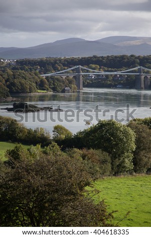 Image of a bridge in North Wales. Anglesy. Image shows bridge over water and country side. Mountains in background. Cloudy day.