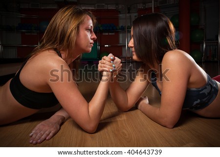 Two young women lies on the floor clutching his hand and looking at each other