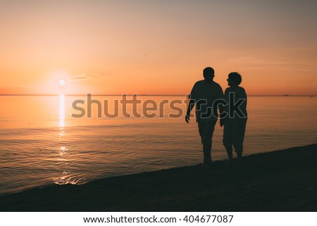 Silhouette of adult couple walks on the seashore against a sunset. Evening photo.