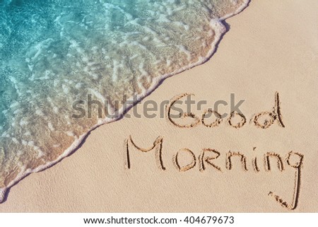 Good morning handwritten on a sandy beach with soft wave of blue ocean on background.