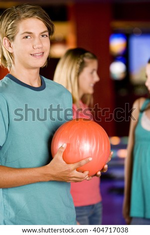 Teenage boy in a bowling alley, two girls in the background